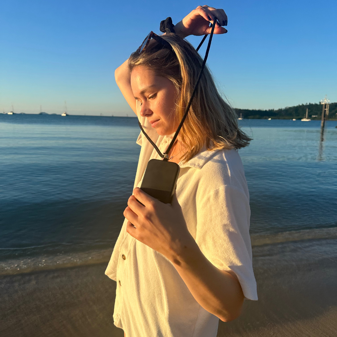 woman wearing a black universal crossbody phone strap at the beach