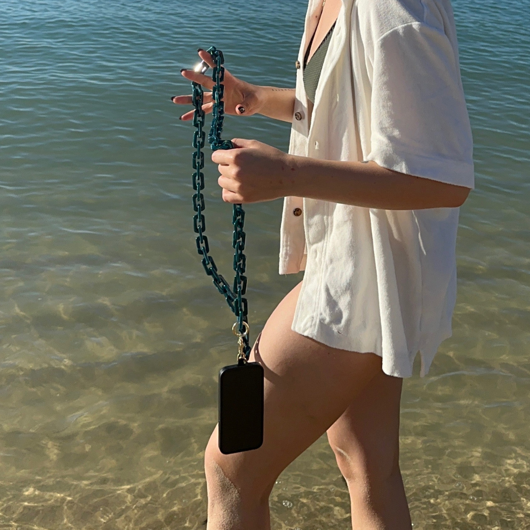blue crossbody phone chain attach to a phone and handle by a women at the beach